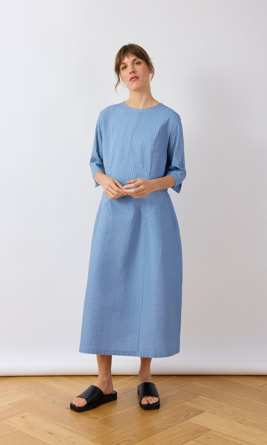 Plümo- Woman in a sky blue Kai Pleated Dress by Yacco Maricard, styled with black slide sandals.