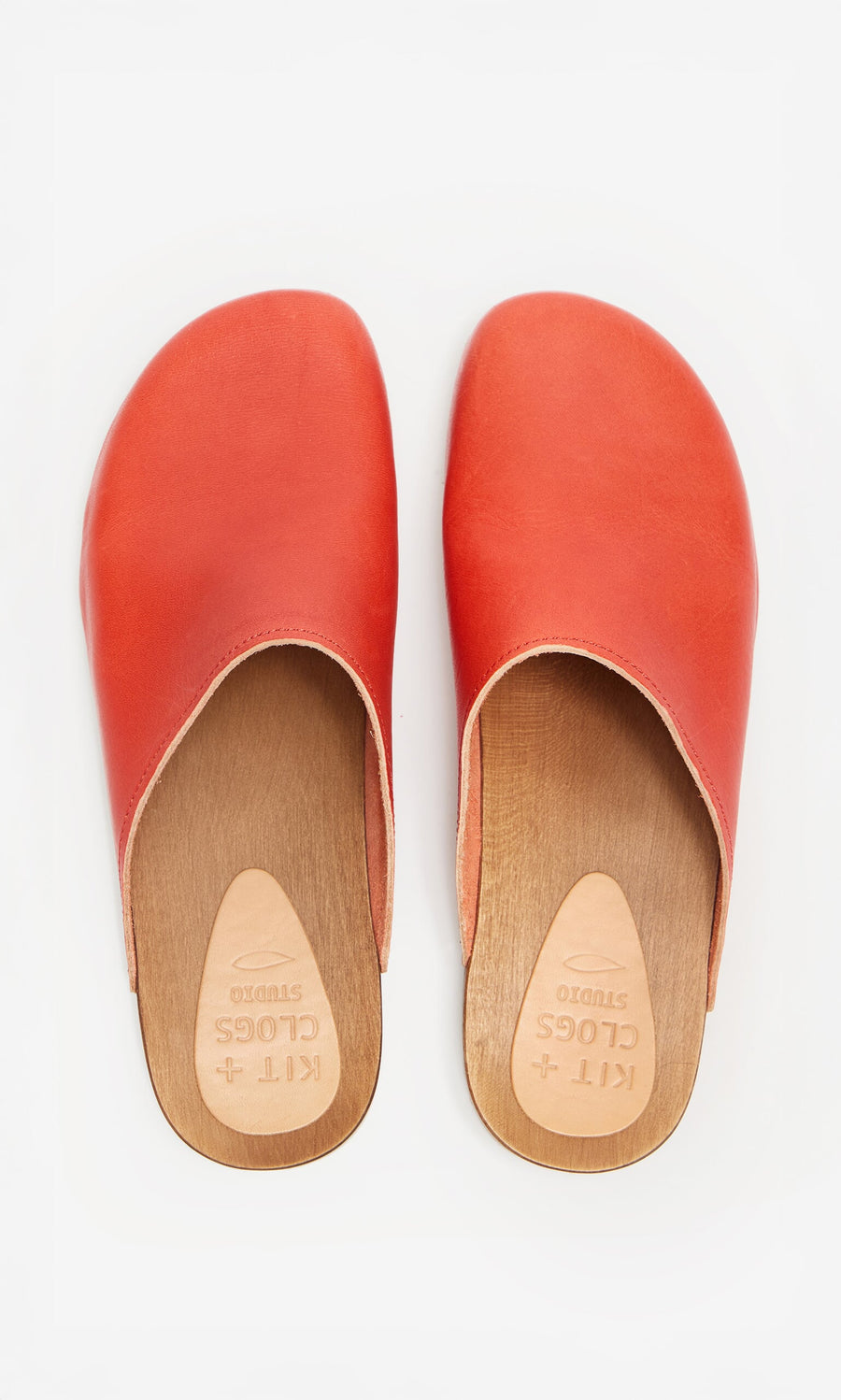 Plümo- Carlie Clogs: orange Swedish clogs in vegetable-tanned leather with wooden soles, shown from above on white.