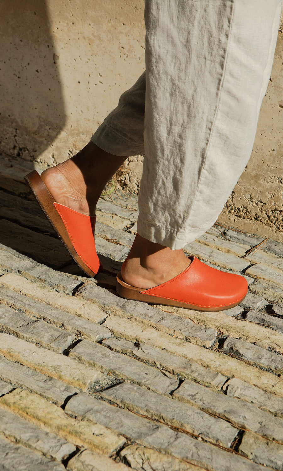 Plümo- Wearing loose light pants and Carlie Clogs, known for ergonomic comfort, a person walks on a sunlit stone path.
