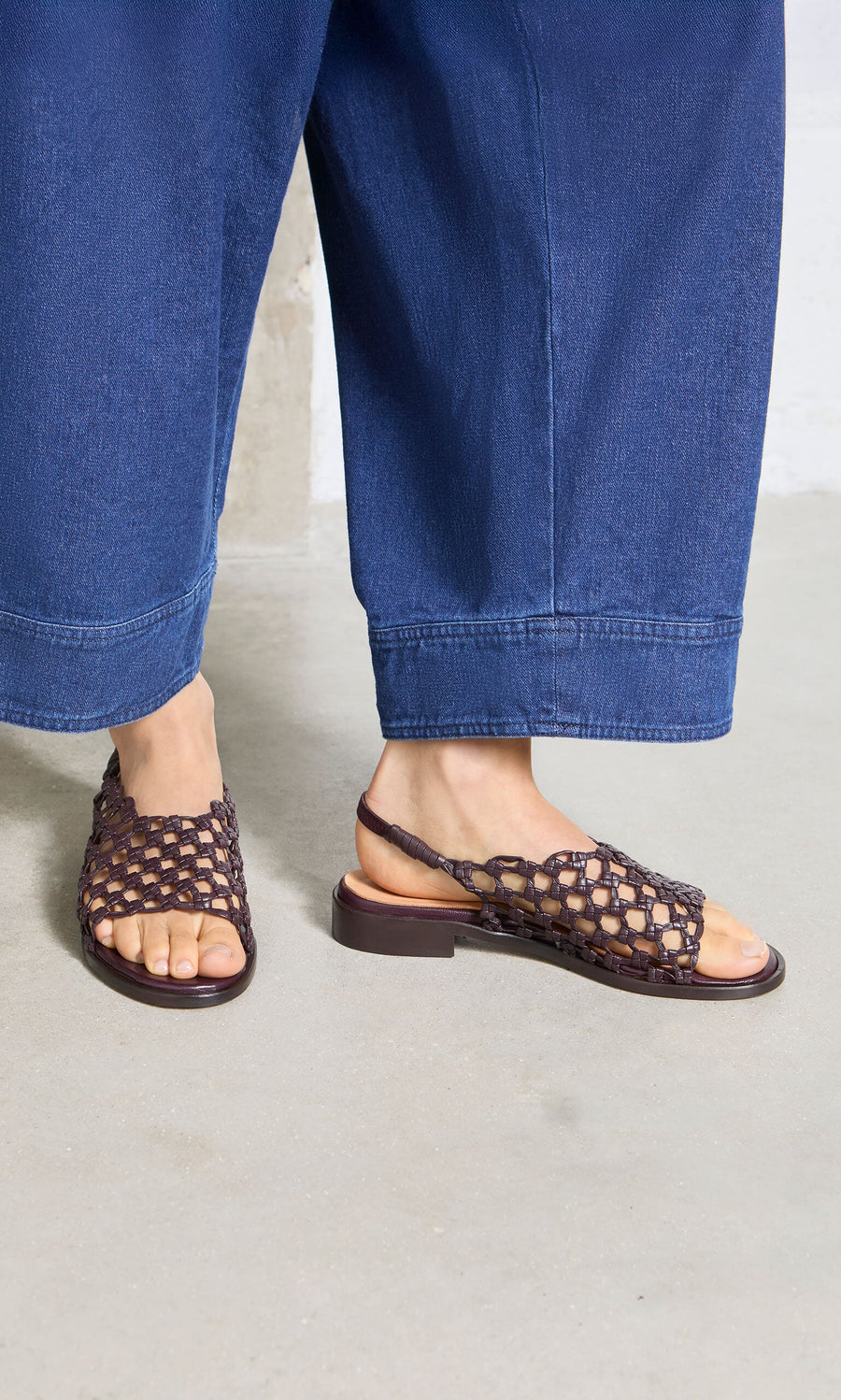 Plümo- Person wearing wide-leg blue jeans and Arts Club Sandals, handcrafted in Spain, on a light-colored floor.