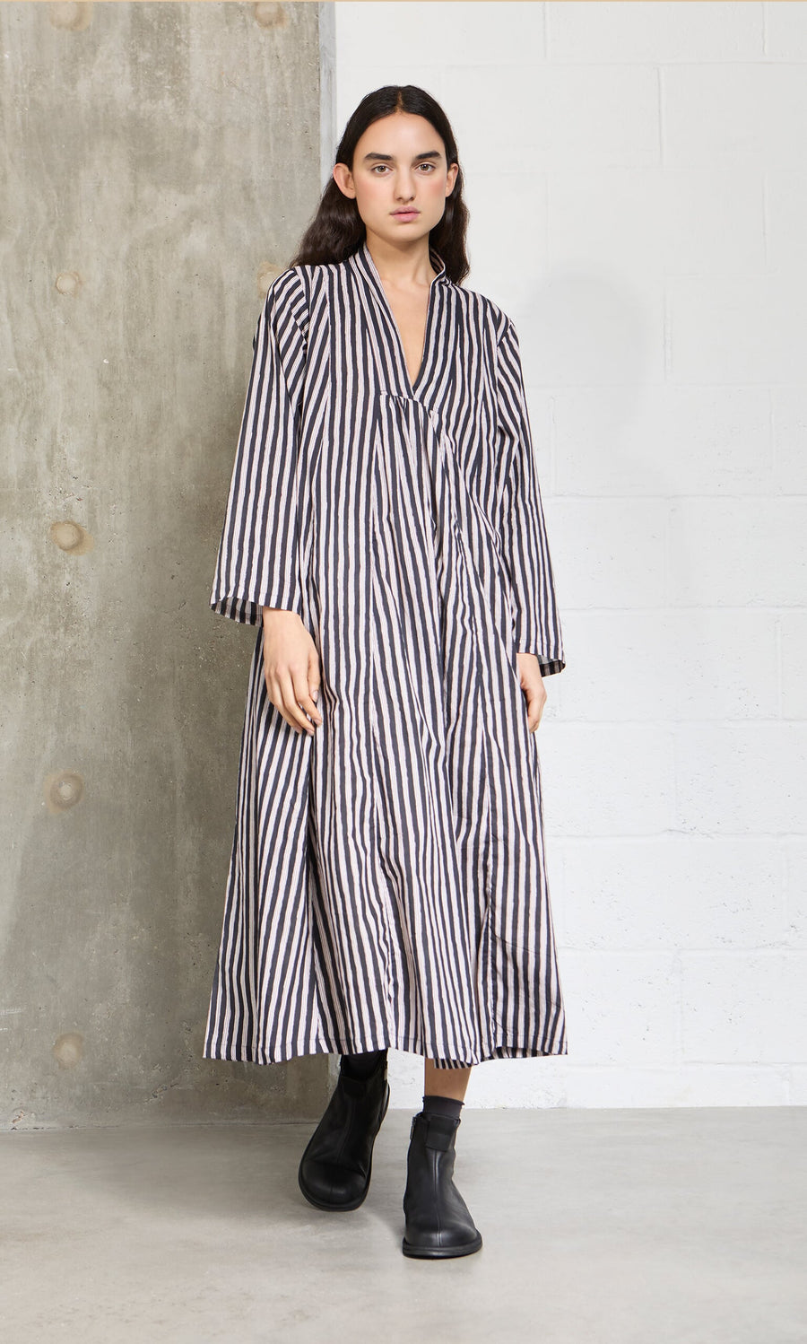 Plümo- Indoors, a woman wears the Hoyland Dress - Charcoal Stripe with black ankle boots.
