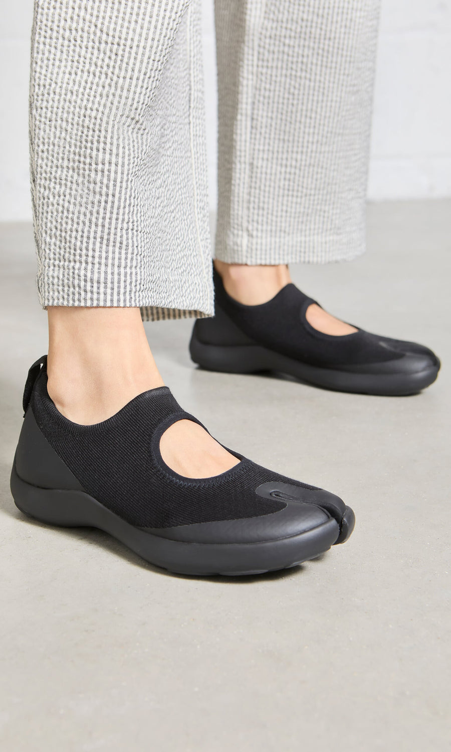 Plümo- Person wears Tabi Sandals in black with white textured pants, standing on a light-colored floor.
