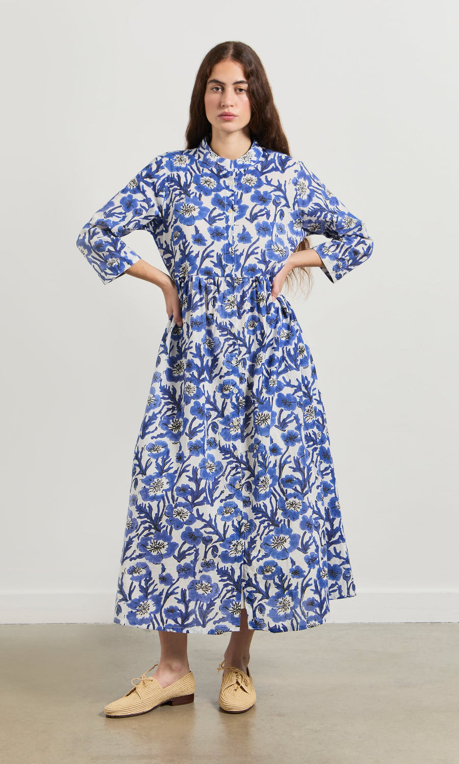 Plümo- Woman in the Blue Pansy Dress, a hand-printed cotton voile dress with blue and white florals and three-quarter sleeves.