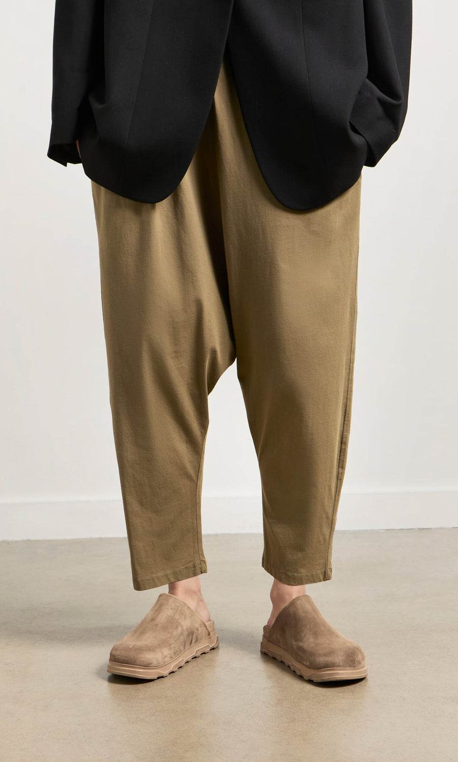 Plümo- Person in loose tan pants, black jacket, and Como Mules with a comfortable moulded footbed on a light floor.