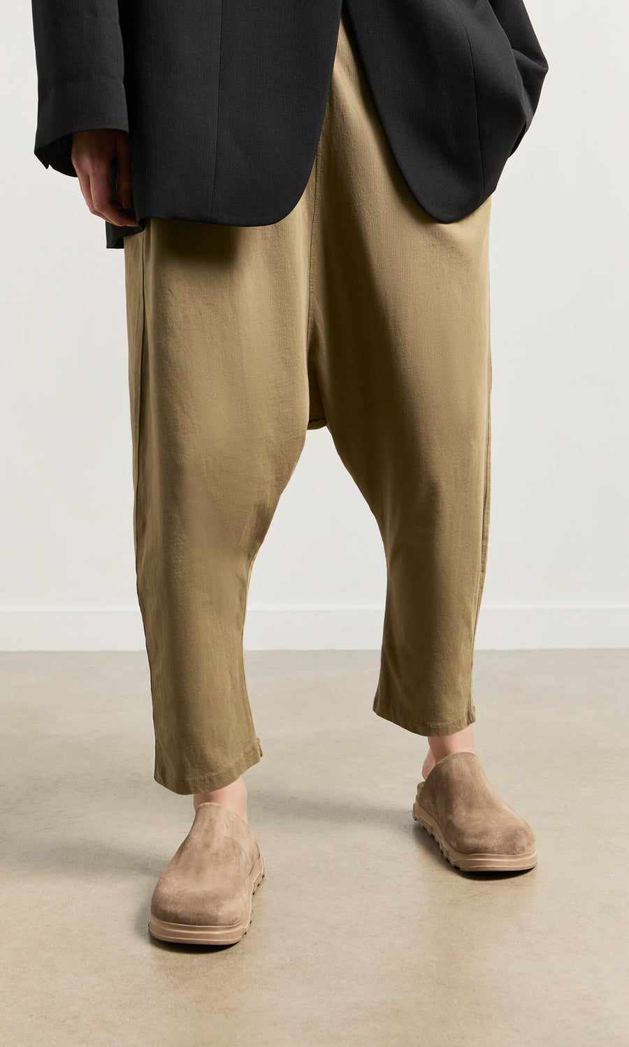 Plümo- Person wearing loose tan drop-crotch pants, black blazer, and Como Mules with a comfortable moulded footbed, indoors.