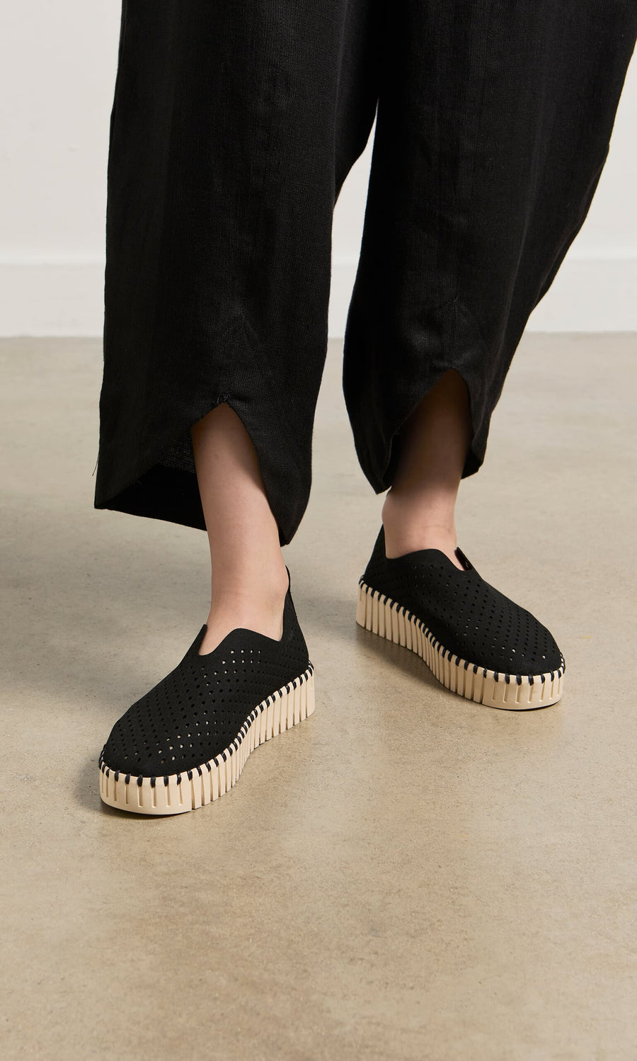 Plümo- A person wearing Tulip Shoes - Carbon with thick white soles and black wide-leg pants.