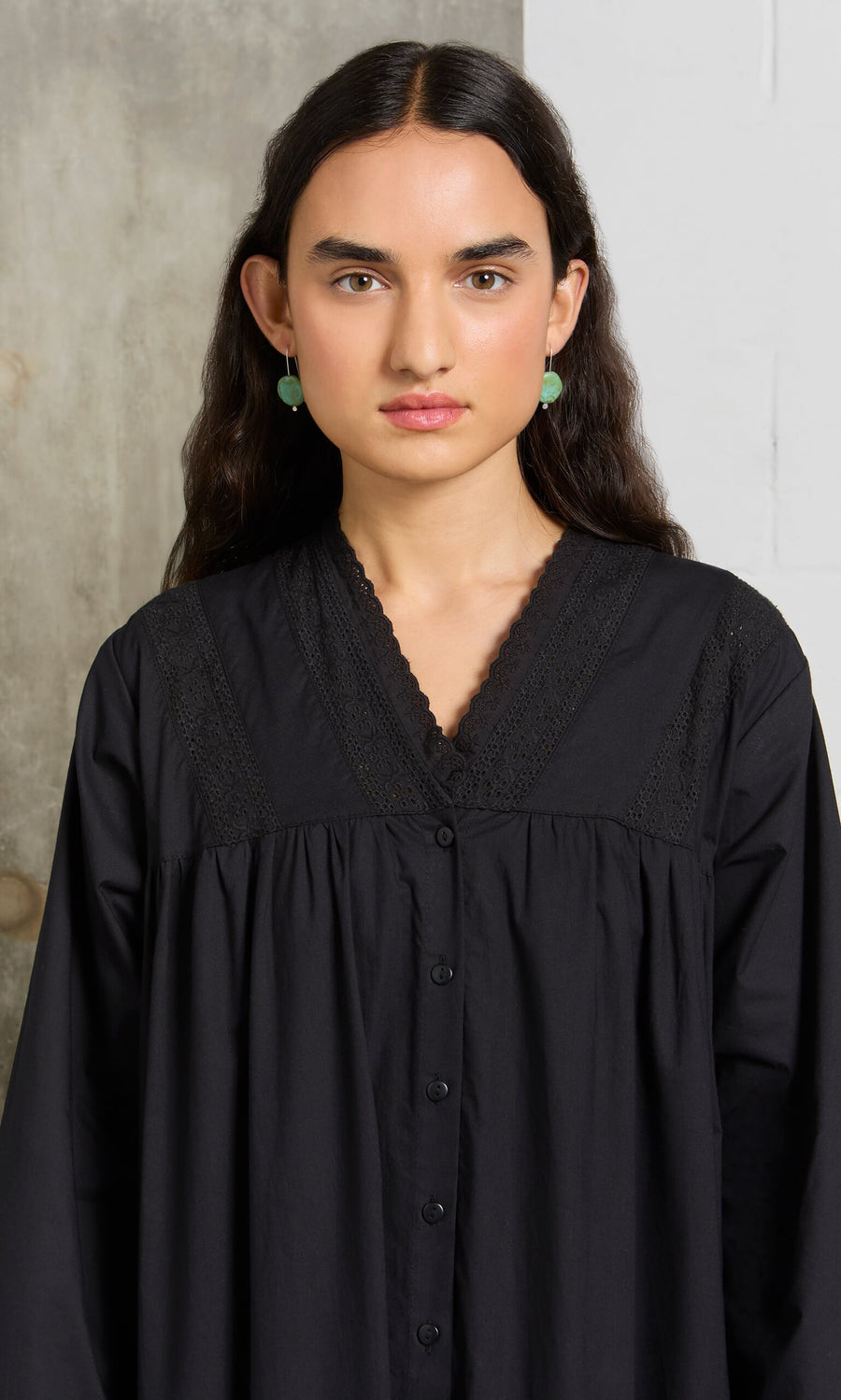 Plümo- Woman with long dark hair wearing the Lily Dress and green earrings, standing against a neutral background.
